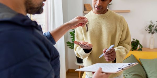 Person handing over keys while another signs a document.