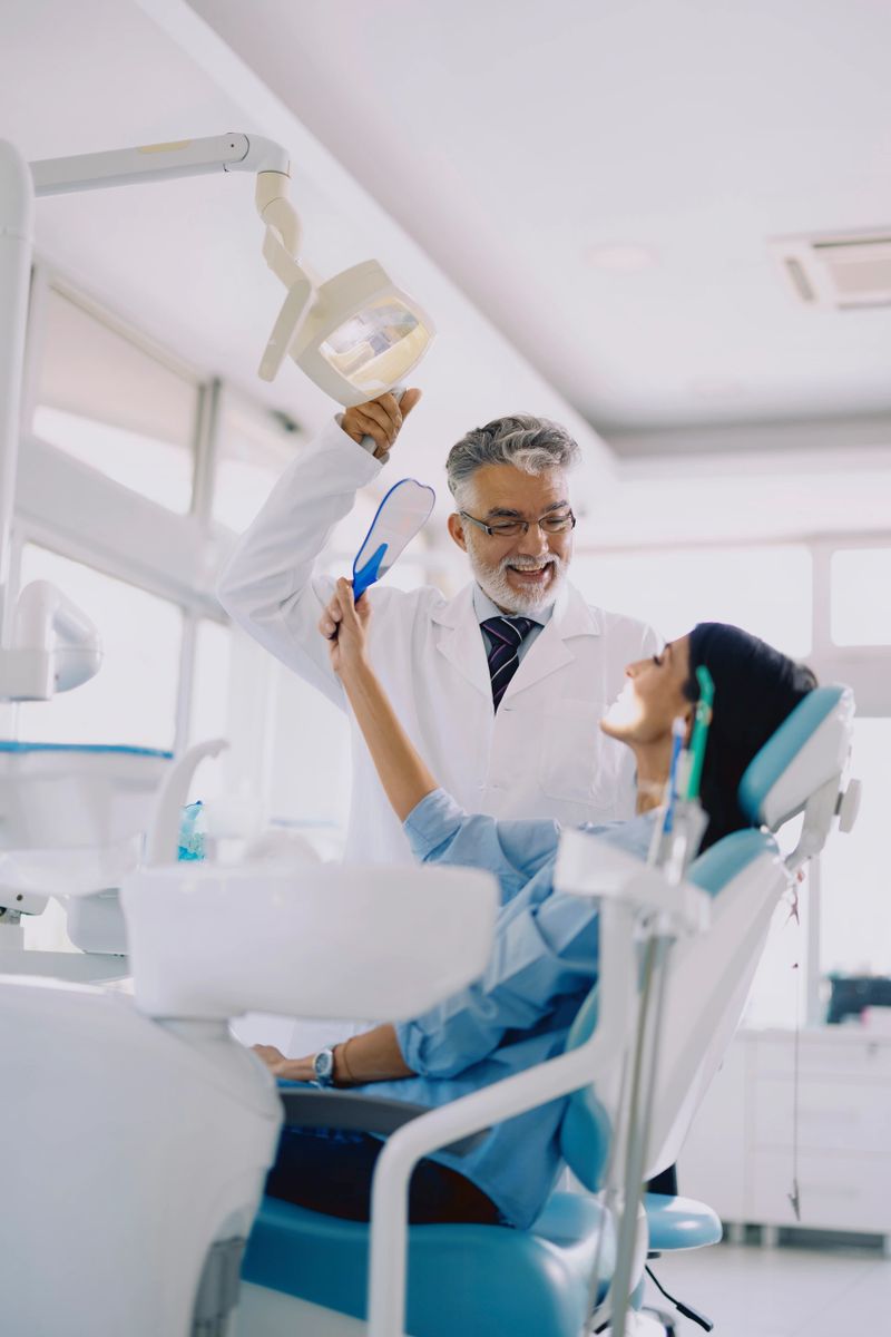 A senior male patient warmly shakes hands with a young female dentist after completing a dental procedure in a modern dental clinic. The dentist smiles in a friendly and professional manner, reflecting trust, satisfaction, and positive patient–doctor communication. The bright, clean dental office interior and visible equipment emphasize a comfortable and professional healthcare environment.