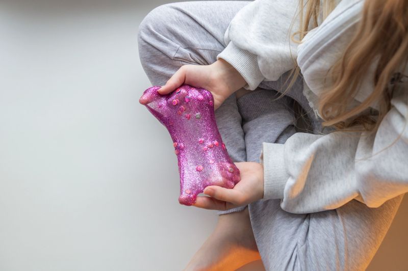 A close up of a small child playing with slime, stretching, squeezing, and exploring its texture