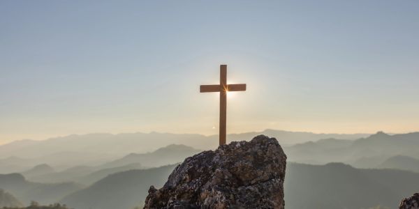 Wooden cross on a rocky peak at sunrise.