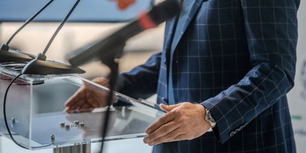Person speaking at a clear podium with microphones.