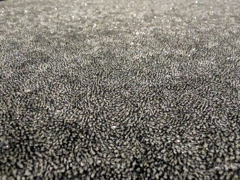 A close up view shows a dark surface with a unique texture. Small sparkles reflect light, creating an interesting visual effect. The setting is indoors during the evening.