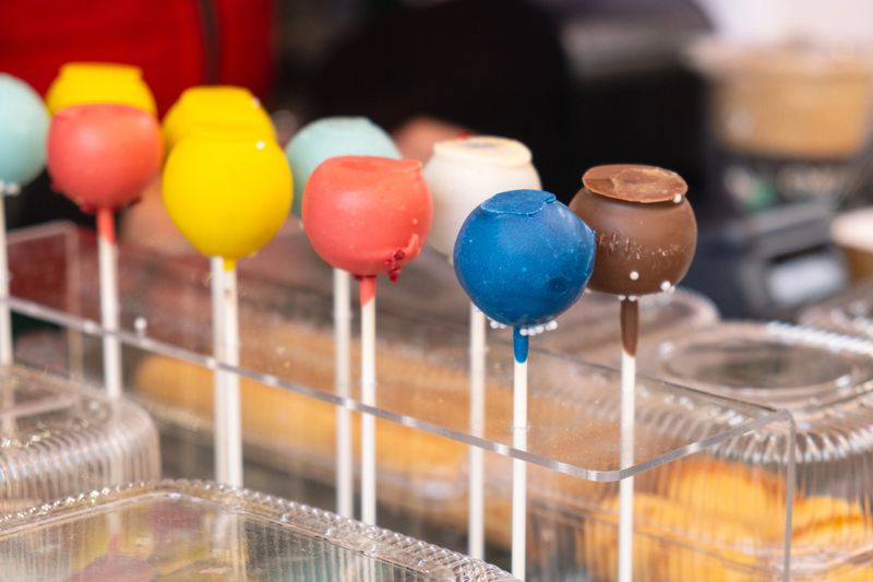 Colorful cake pops in bright candy coating displayed on sticks at dessert stand create playful street food scene, perfect for bakery advertising, children party promotions, and food festival marketing