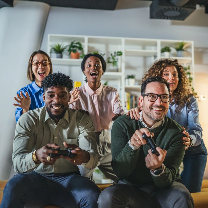 Enthusiastic multicultural group of adult friends gathering in a modern living room, playing a video game, making excited facial expressions, and having fun during a social activity