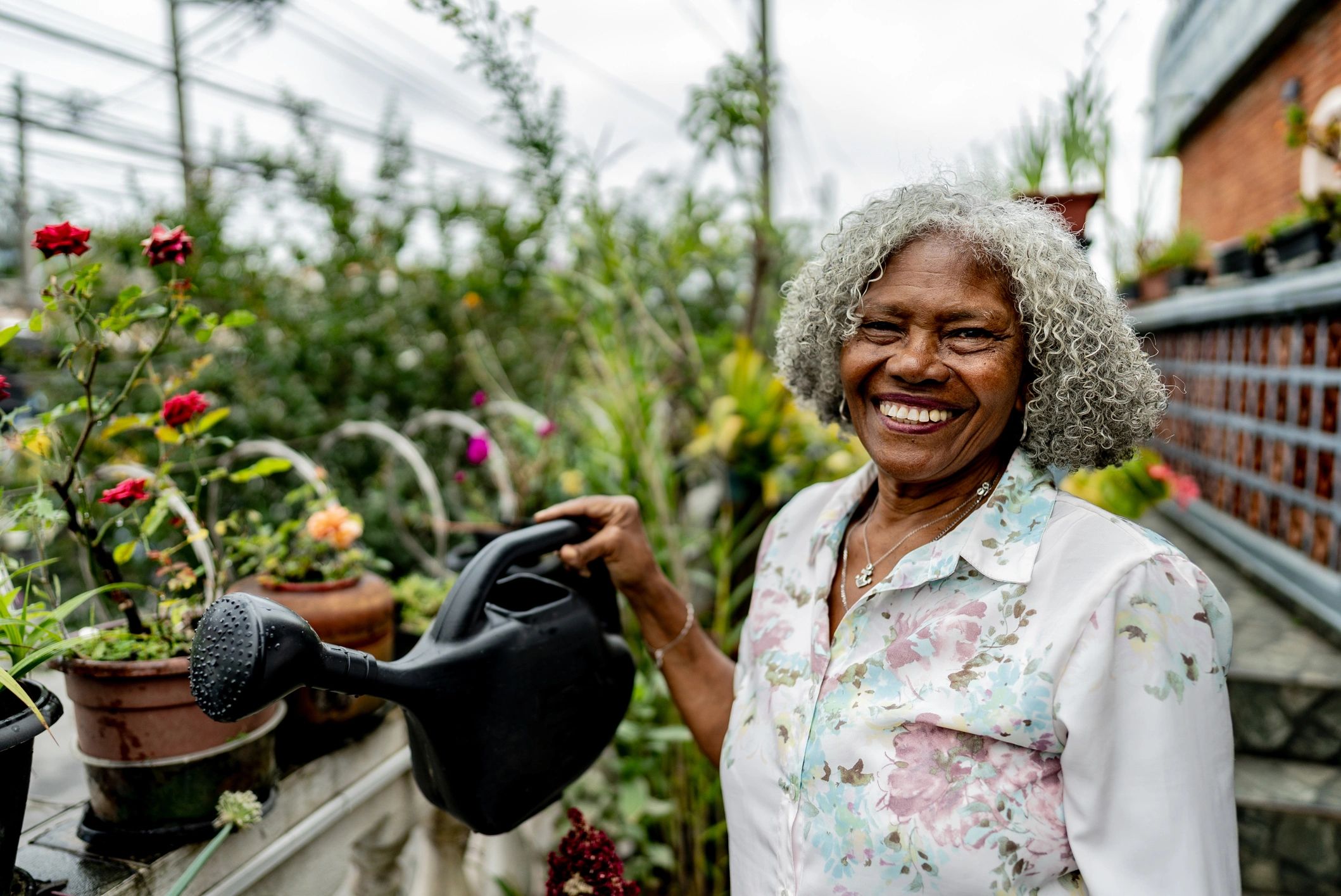 Elderly woman smiling while watering plants in a garden.