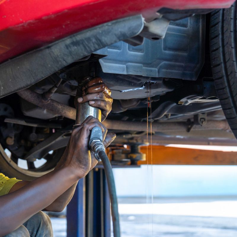 Auto mechanic draining transmission fluid from a vehicle during an ATF or Automatic Transmission Fluid oil change. Automotive maintenance, car repair and service concept.