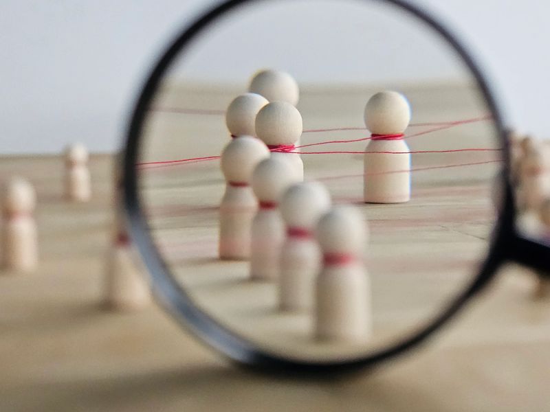 Wooden figures of people are connected by a network of red threads. Contacts between participants, staff, and the community. Social media and communication