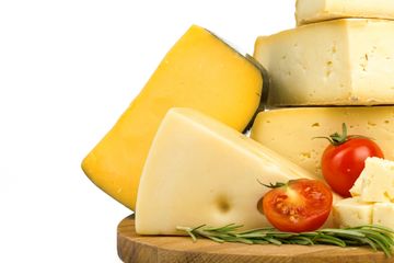 Variety of cheeses with cherry tomatoes and rosemary on wooden board.