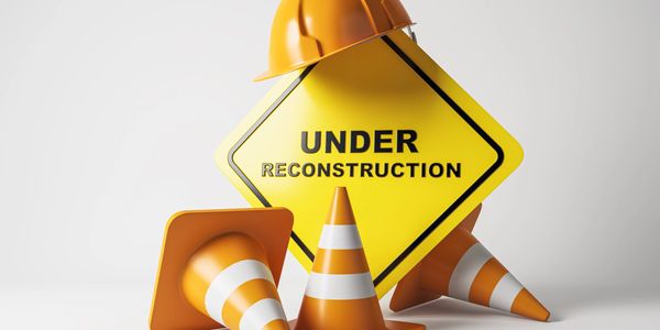 Construction cones and a hard hat around an under reconstruction sign.