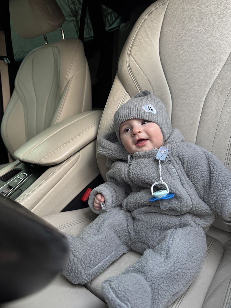 Happy baby wearing knit hat and cozy winter suit sitting in car