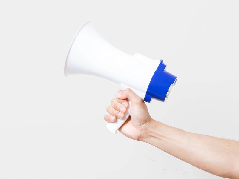 Hand holding a megaphone on a clean background, symbolizing announcement, alert, promotion, public message, and communication.