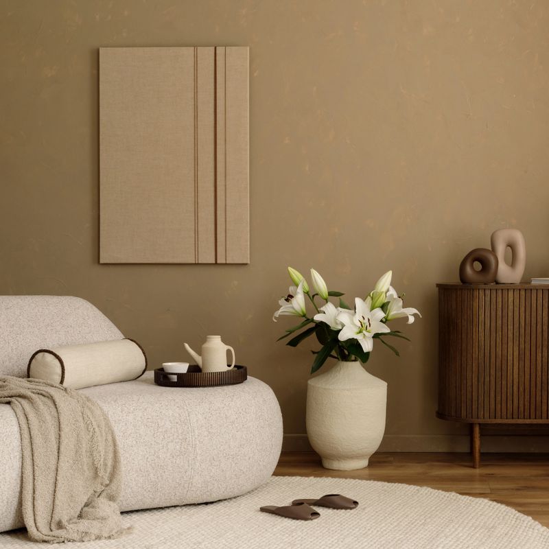 Neutral toned living room with soft boucle sofa, sculptural decor, white lilies,  mock up art work and a wooden cabinet against a beige wall.