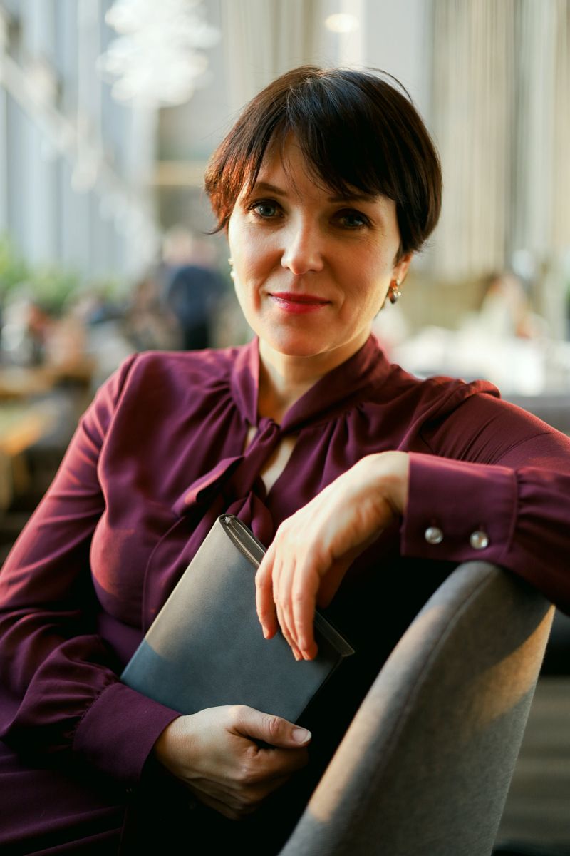 A confident woman holds a notebook while sitting in warm natural light, creating a professional portrait ideal for coaching, consulting, business branding, and corporate identity projects.