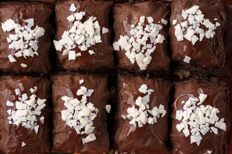Squares of rich chocolate brownies are arranged in a neat grid. Each brownie is generously topped with shredded coconut, creating a tempting dessert presentation.
