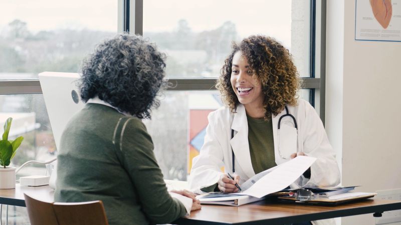 A female doctor smiles while talking with a patient in a bright, modern medical office.