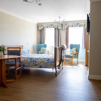 A bright and airy bedroom with wooden floor, white bedding and curtains, with touches of blue. 