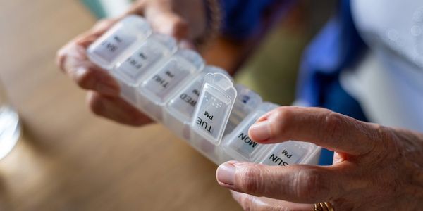 Hands holding a weekly pill organizer with compartments labeled by day and time.