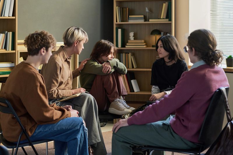 Group of diverse young people and teenagers sitting in circle participating in group therapy session, multiethnic people in supportive conversation in counseling setting