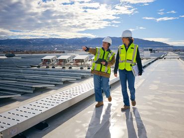 Two construction workers in safety gear inspect solar panels on a rooftop.
