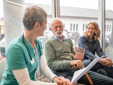 Elderly man talking with a nurse and a woman in a waiting room.