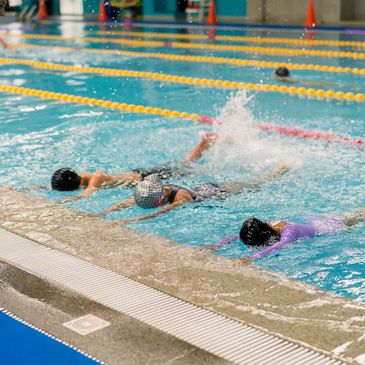 Three swimmers practicing backstroke in a pool with lane dividers.