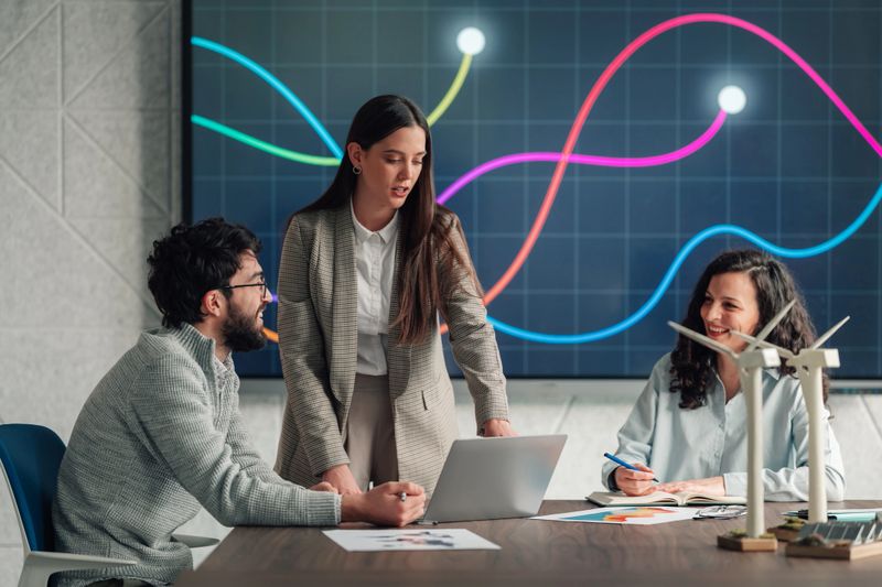 Professionals collaborating on sustainable development ideas, using a laptop and a large screen displaying charts