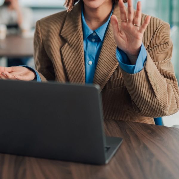 Person in brown jacket talking on video call with laptop.