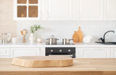 Wooden cutting board on a kitchen counter with white cabinets.