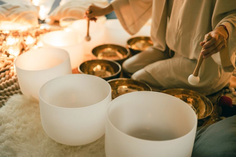 Close-up of a person using mallets to play crystal and metal singing bowls in a soft, glowing meditation space, creating a peaceful environment for sound healing and deep relaxation.