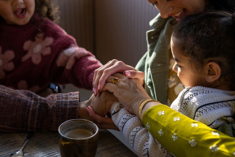 Medium shot of a family enjoying time together at a cafe. Focus is on their hands, which they are all stacking, holding each other. The cafe is located in Northumberland, England. The family are muslim. Videos are available similar to this scenario.
