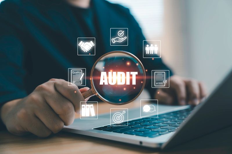 Businessman holding magnifying glass with audit wording and icons for quality management compliance evaluation and document review showing the concept of professional inspection and organization