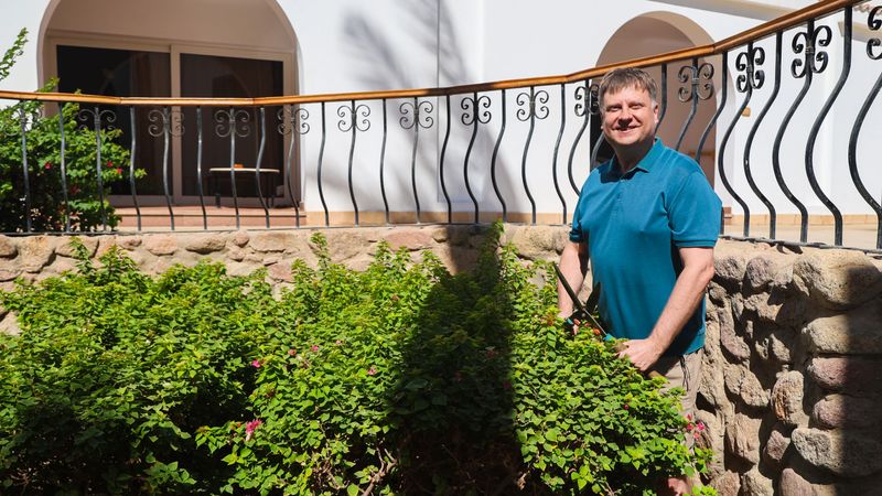 Adult Man Pruning Bushes in His Garden with Shears, Enjoying a Productive Day at Home Surrounded by Lush Greenery Nature.