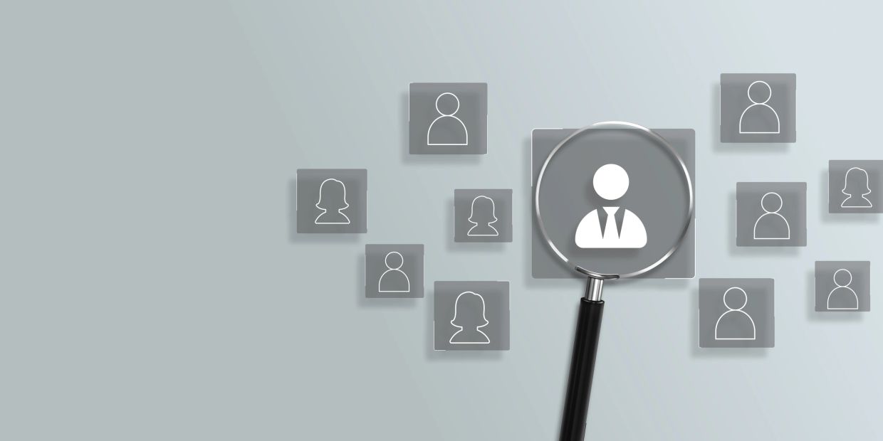 Magnifying glass highlighting a business professional icon among others.
