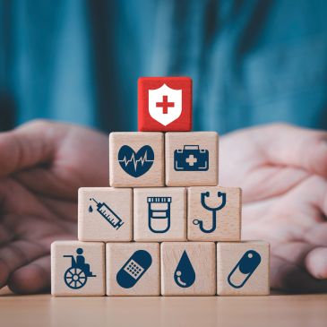 Healthcare icons on wooden blocks stacked in pyramid with hands protecting.