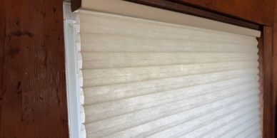 A closed white pleated window blind with wooden frame.