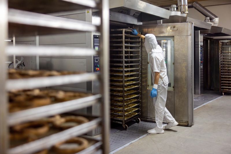 Latin American baker taking trays of bread out of the oven while working at an industrial bakery