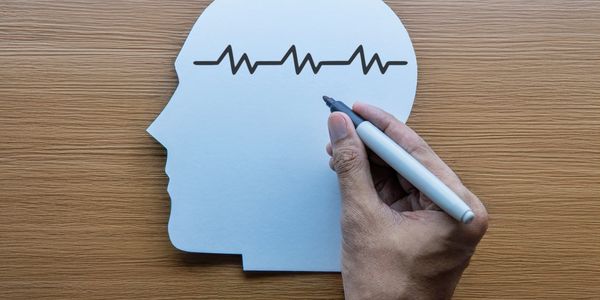 Hand drawing brainwave inside head silhouette.