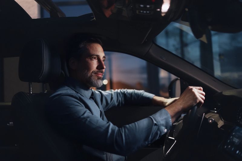 A focused, professional man drives a car at night, showcasing corporate travel and night work. The modern vehicle interior emphasizes concentration, control, and a calm, confident mood.