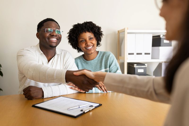 Happy couple shaking hands with financial advisor after signing contract in office