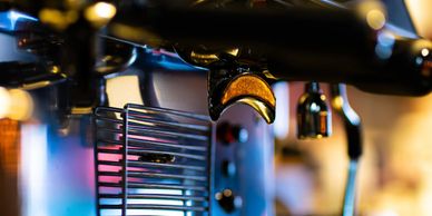 Close-up of a modern espresso machine's portafilter and drip tray with colorful lighting.