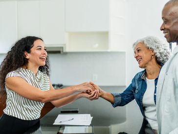 Two women smiling and shaking hands across a table.