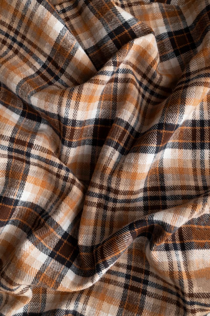 Wrinkled in folds plaid brown orange beige flannel cotton fabric, tartan pattern. Close-up of this autumnal natural fabric for shirt, dress, tablecloth, or clothing. Abstract textile background