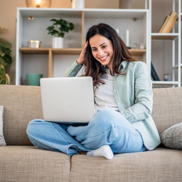Mujer sonriente usando laptop en el sofá.