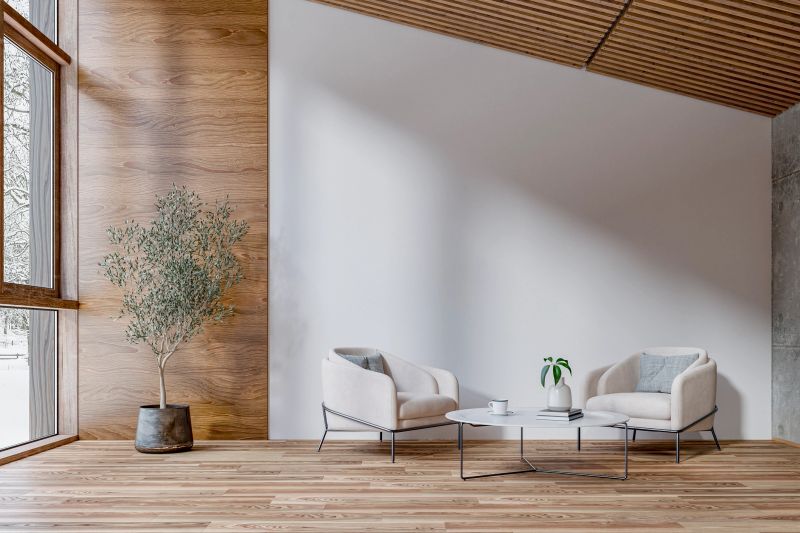 A modern living room in a log cabin features a  pair of white cozy armchairs and side table (with a book and coffee cup, vase with a flower) set against a clean, minimal wall. To the left, a large potted plant - olive tree stands beside large windows showcasing a snowy outdoor scene. Warm wooden elements on the floor and wall add natural contrast and create a cozy, inviting atmosphere. A 3D rendered image.