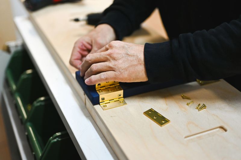 Person attaching a brass hinge to a piece of wood on a workbench, making custom furniture
