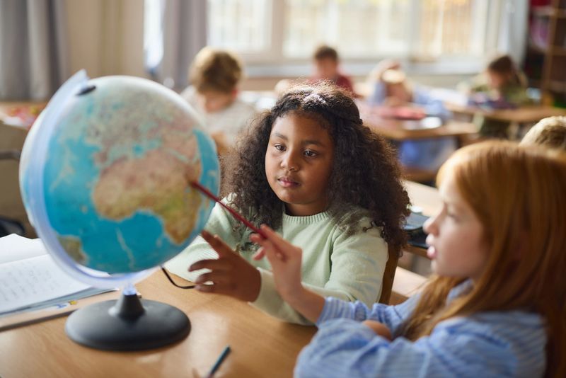 Diverse schoolgirls cooperating while examining the globe during a class at elementary school.