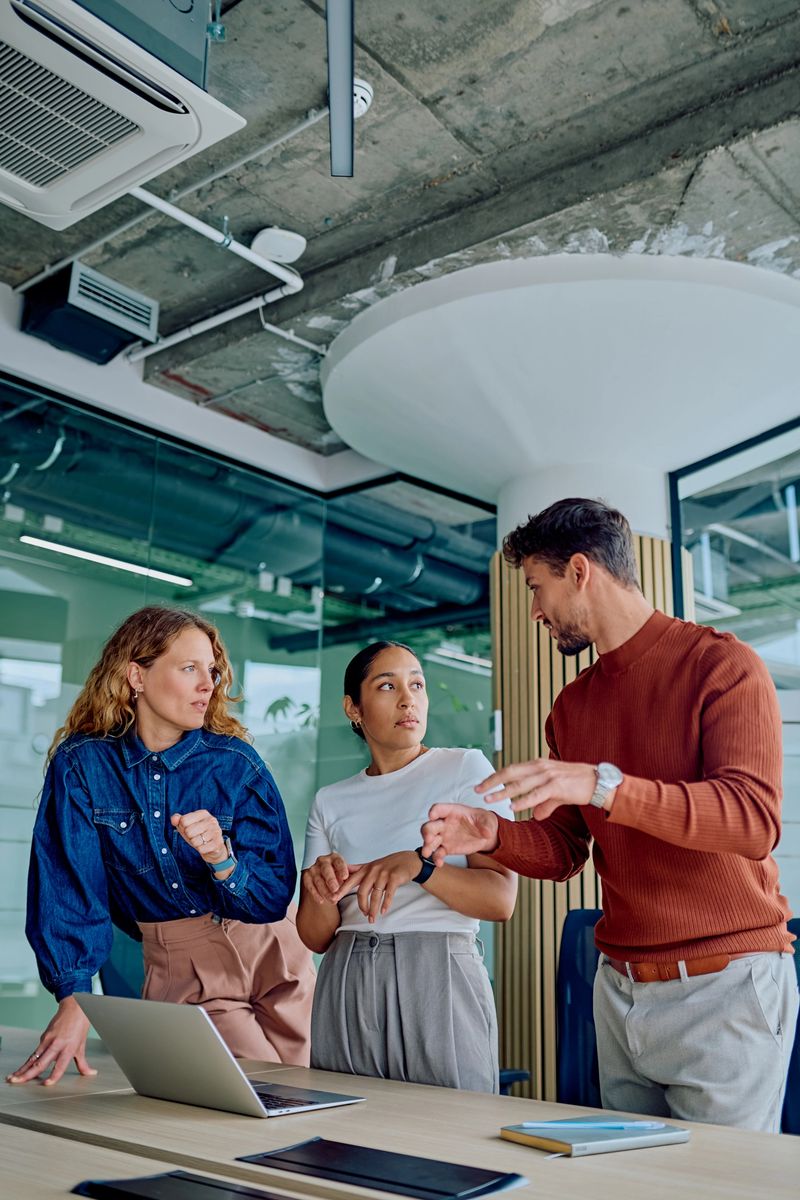 Three diverse business people collaborating, sharing ideas, and planning strategies during a team meeting in a contemporary workspace