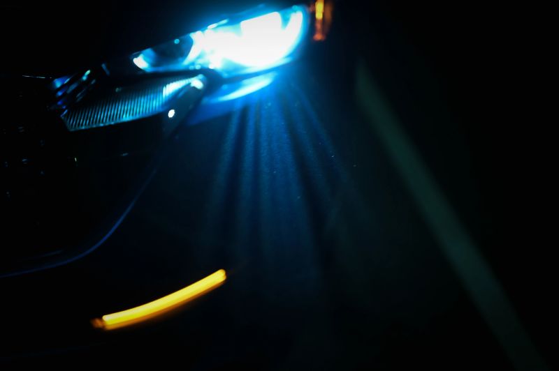 Car headlight shining blue light in darkness, creating abstract light rays and glow