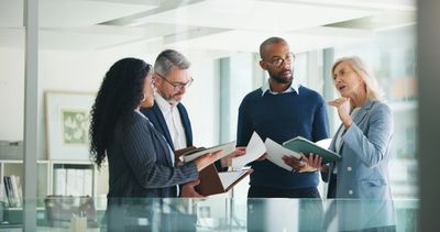 Réunion d'affaires avec quatre collègues discutant de documents.
