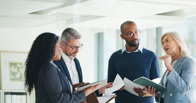 Four professionals engaged in a discussion with documents and notebooks.